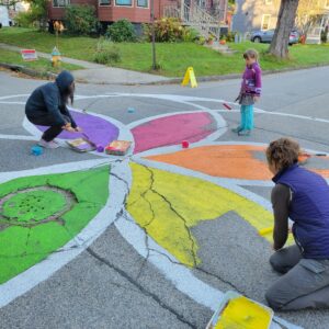 Three people paint a colorful design on the street